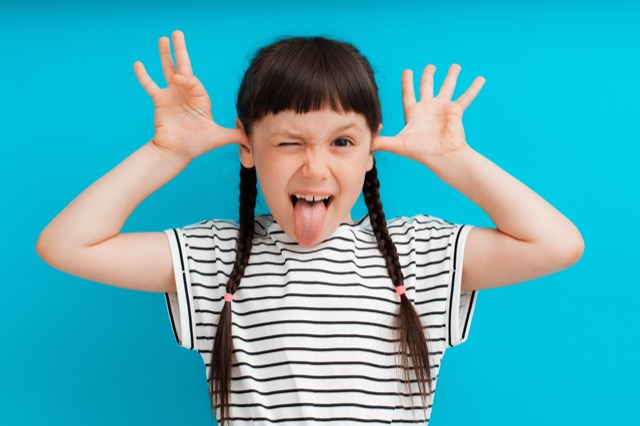 portrait of a child girl happy positive smile shows a grimace stuck out tongue isolated on a blue background spread fingers.