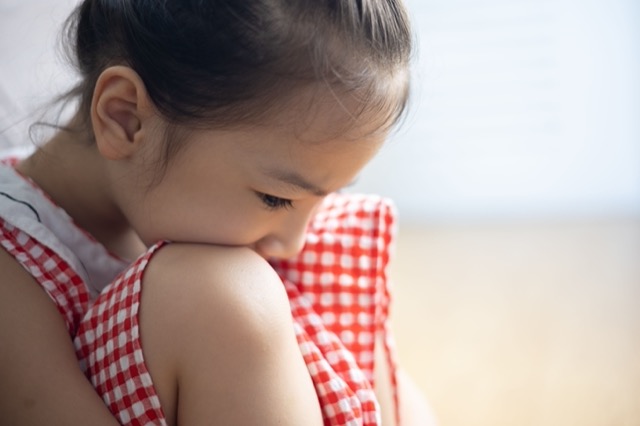 Face close up of cute asian kid girl is sitting on the bedroom floor with sorrow, depressed, upset and scared expression which is due to family punishment and violence, and this is the social problem.